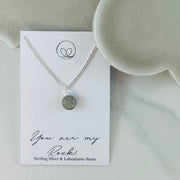 Sterling silver necklace with a round Labradorite stone, symbolizing strength and stability. Displayed on a 'You Are My Rock' background. Includes an 18” curb chain.