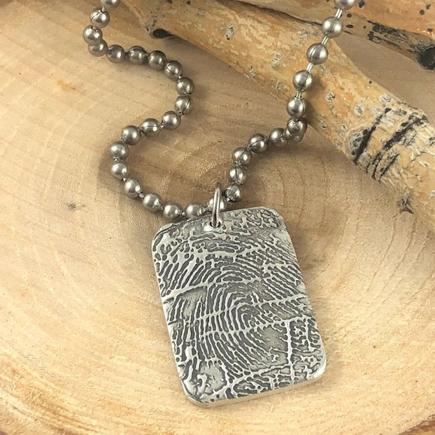 Fine silver fingerprint dog tag pendant, a personalized keepsake crafted from a loved one's print, using paper or digital impressions for a timeless tribute.