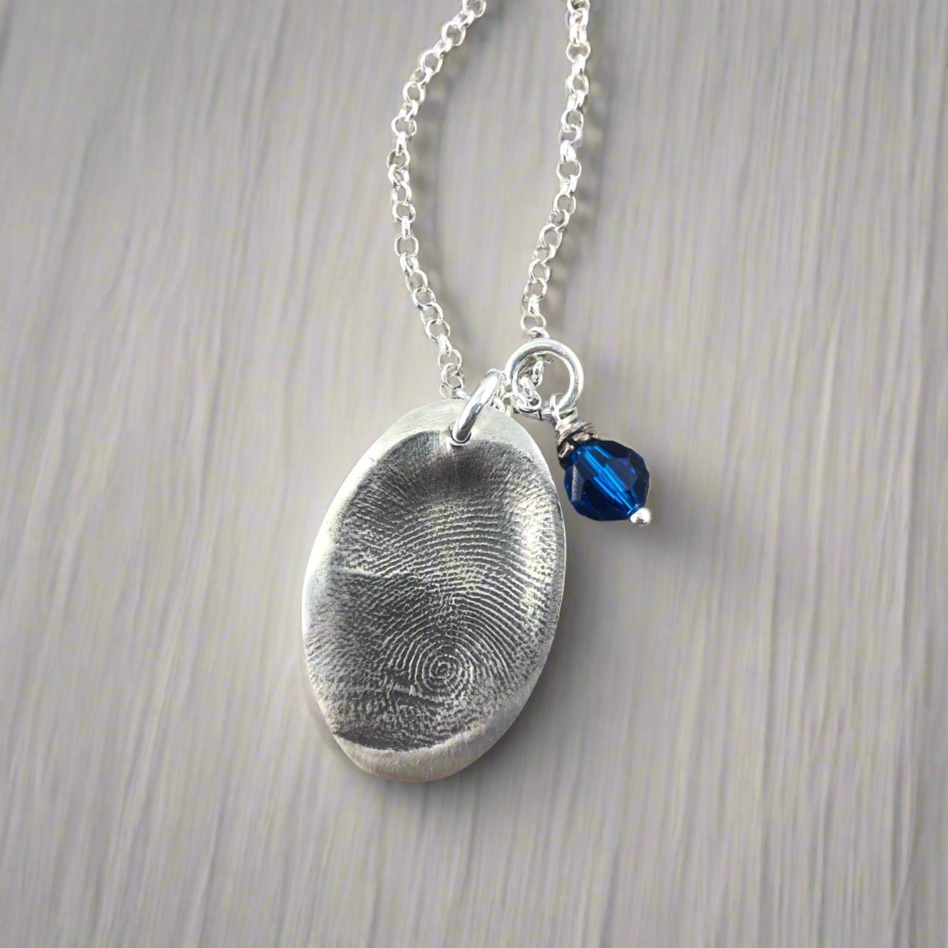 Oval fingerprint pendant crafted in fine silver, featuring a detailed replica of a fingerprint for a unique and personalized keepsake.