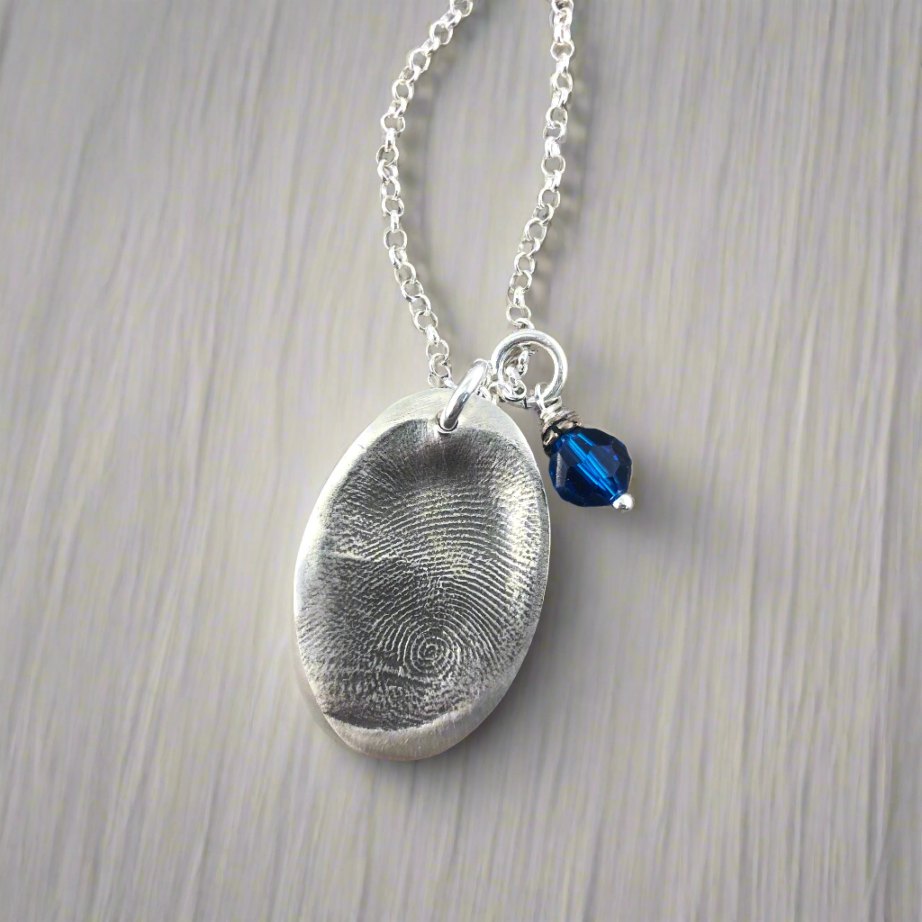 Oval fingerprint pendant crafted in fine silver, featuring a detailed replica of a fingerprint for a unique and personalized keepsake.