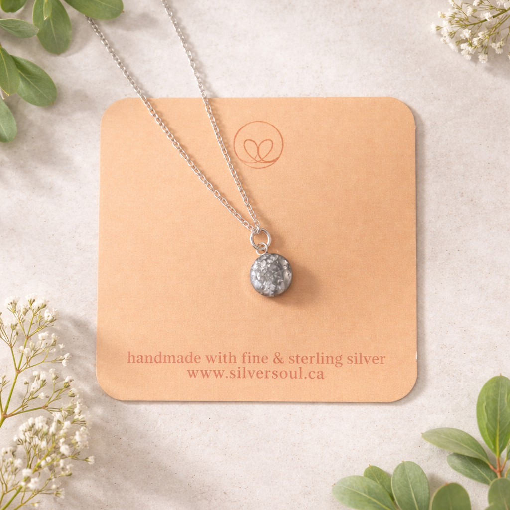 Necklace with a silver pendant on a beige card with greenery around