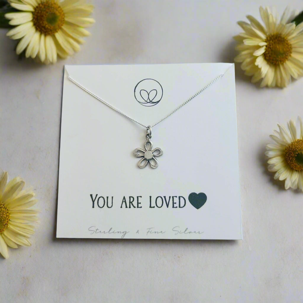 Silver flower necklace on a 'You are Loved' card with a white background