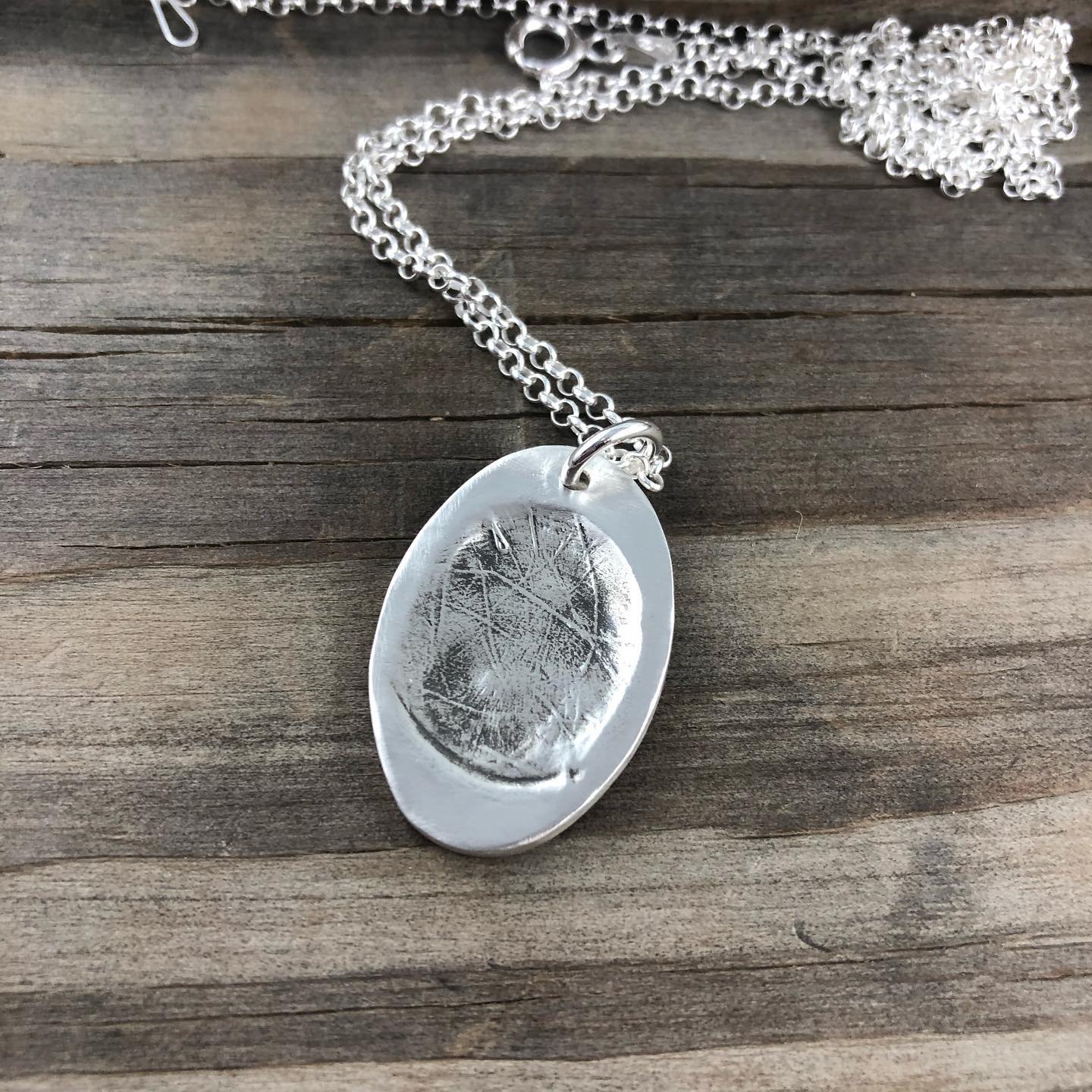 Oval fingerprint pendant crafted in fine silver, featuring a detailed replica of a fingerprint for a unique and personalized keepsake.








