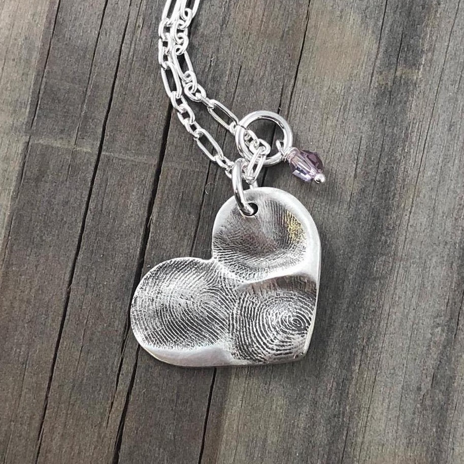 Handcrafted heart shaped fine silver pendant featuring 1-3 loved ones' prints, a modern alternative to a family ring for a sentimental and timeless keepsake.