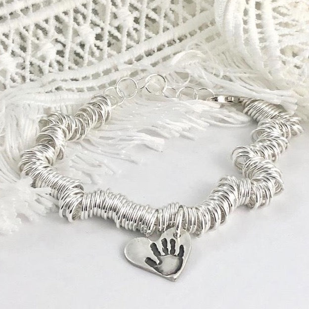 Sterling silver charm bracelet featuring hundreds of rings for elegant movement. Customizable with charms on lobster clasps for easy arrangement.